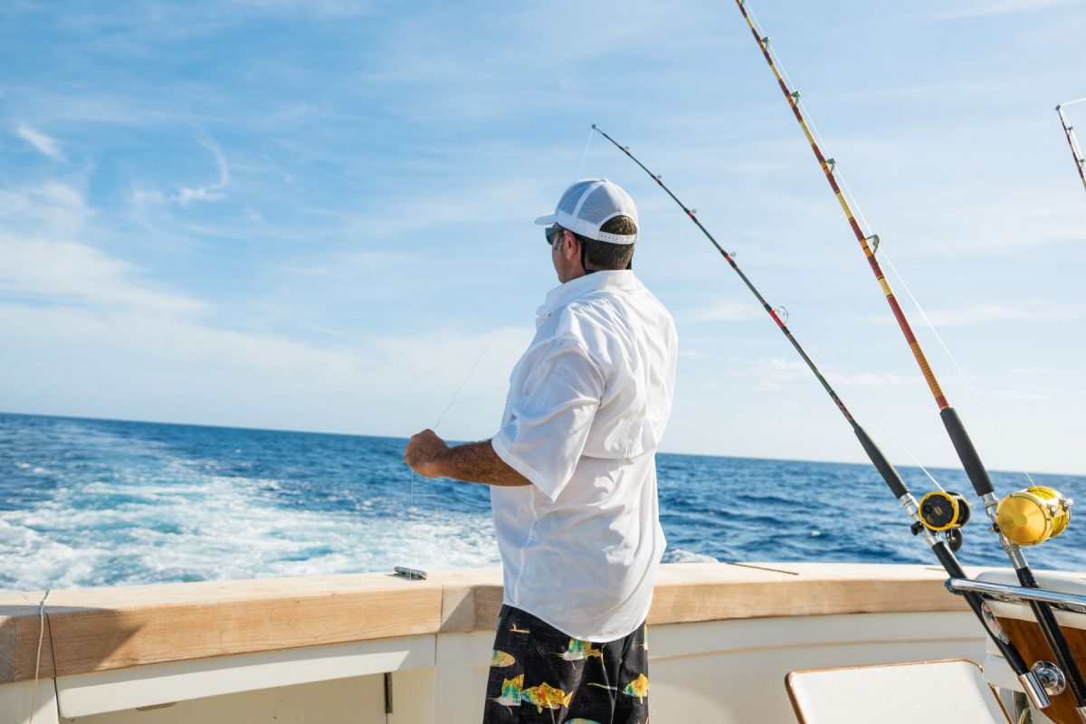 Man on a chartered fishing boat next to several deep sea fishing rods